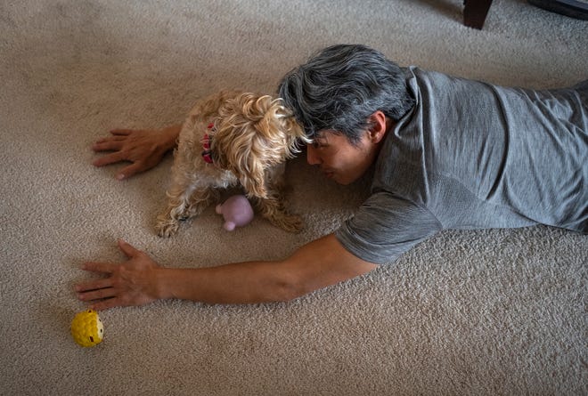 Jeffrey Wu, 47, of Lakeville, Minnesota, is interrupted by his dog, Willy, wanting to play as Wu stretches at his home before going to sleep after his late-night shift at a dairy plant on Wednesday, December 6, 2023.