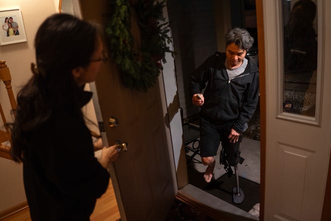 Ting Yang, 41, of Lakeville, Minnesota, gets the door for her husband, Jeffrey Wu, 47, at their home on Tuesday, December 5, 2023, while letting their dog outside before Wu takes a short nap prior to working a late-night shift. Wu had part of his leg amputated after his Jeep rolled back on him at a gas station, crushing his leg. Wu said he thought he put his 2014 Jeep Grand Cherokee - which had an unrepaired safety recall - into park, but instead, it rolled backward and struck him on March 4, 2022.