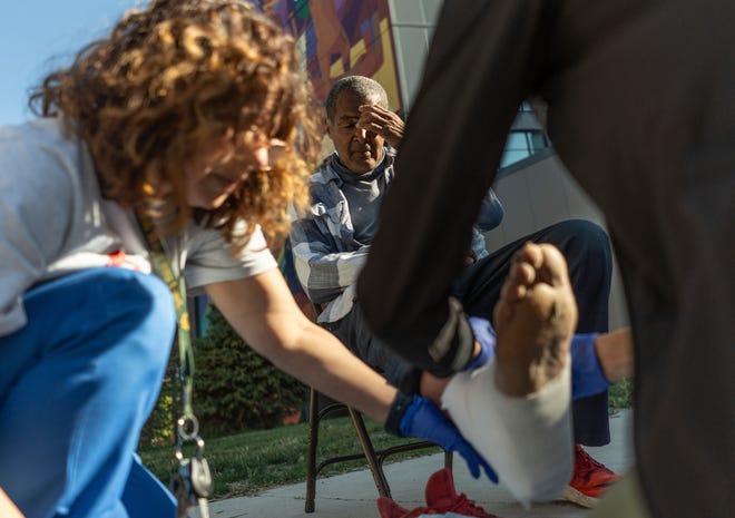 Community Health and Social Services family medicine physician Dr. Shaina Shetty, right, and CHASS family nurse practitioner Danny Diaz, left, wrap the foot of Daniel Lewis, 60, of Detroit, after tending to an open wound while doing street medicine outreach on Monday, August 12, 2024, at Manna Community Meals in Detroit's Corktown neighborhood. CHASS recently received $562,868 in American Plan Act dollars to expand its street medicine team, to aid people experiencing homelessness on the streets taking medical care right to the people who need it.