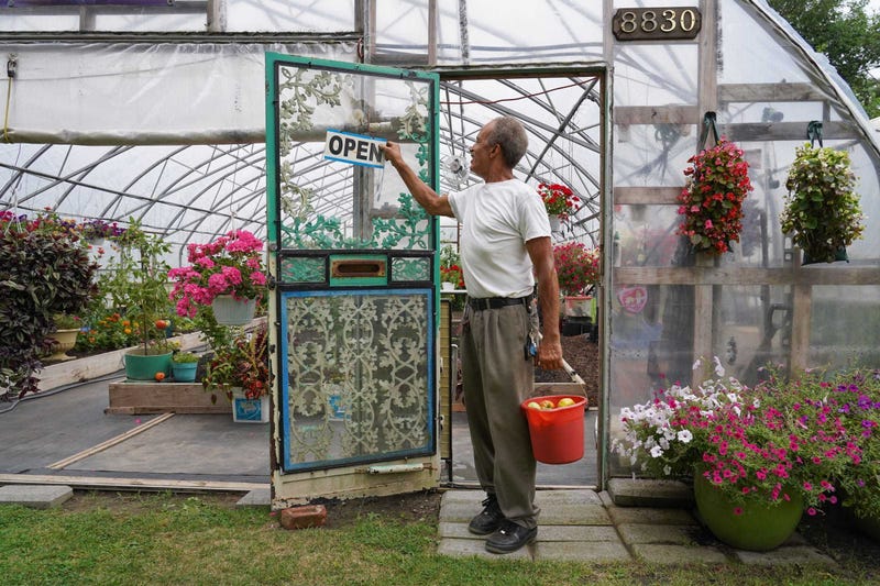 Bill Walton of Detroit changes his sign to read that his business is open while carrying a bucket of vegetables he harvested from one of his gardens while working in a neighborhood in Detroit's east side on Sept. 3, 2019.